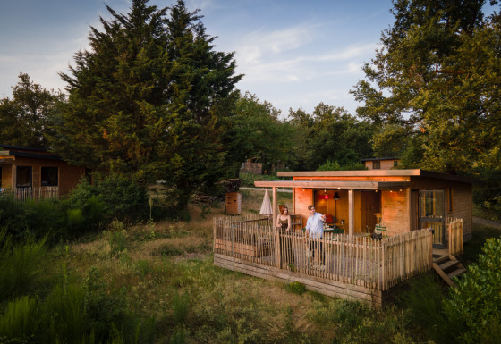 Glamping-Unterkunft Village Huttopia Pays de Condrieu, Holzchalet mit Terrasse in grüner Naturumgebung.