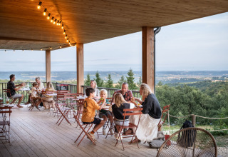 Mensen dineren buiten bij Village Huttopia Pays de Condrieu, met uitzicht op het landschap van Auvergne-Rhône-Alpes.