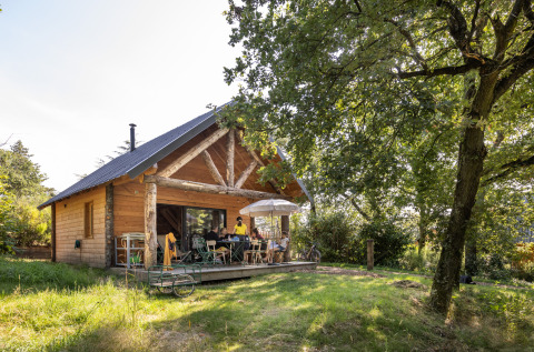 Cabane en bois au Village Huttopia Pays de Condrieu avec des personnes sur la terrasse, glamping Auvergne-Rhône-Alpes.