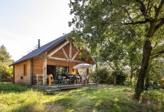 Casetta in legno al Village Huttopia Pays de Condrieu con persone in veranda, glamping in Auvergne-Rhône-Alpes.