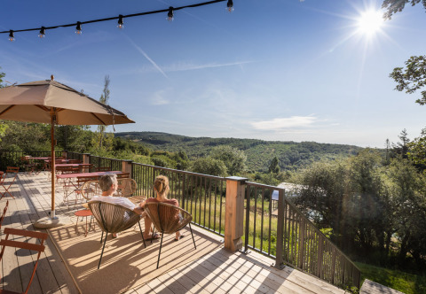 Twee mensen ontspannen op het terras met uitzicht bij Village Huttopia Pays de Condrieu glamping in de natuur.