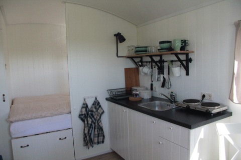 Compact kitchen and bed in a glamping caravan at Campingplatz am Nordseestrand - Zigeunerwagen Oost-Friesland.