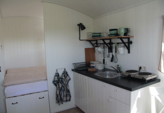 Glampingindkvarteringens lille køkken og soveområde på Campingplatz am Nordseestrand - Zigeunerwagen Oost-Friesland.