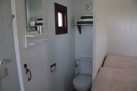 Vue intérieure du glamping Zigeunerwagen Oost-Friesland avec lit, toilettes et miroir au Campingplatz am Nordseestrand.