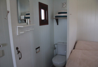 Innenansicht des Zigeunerwagen Oost-Friesland Glamping mit Bett, Toilette und Spiegel auf dem Campingplatz am Nordseestrand.