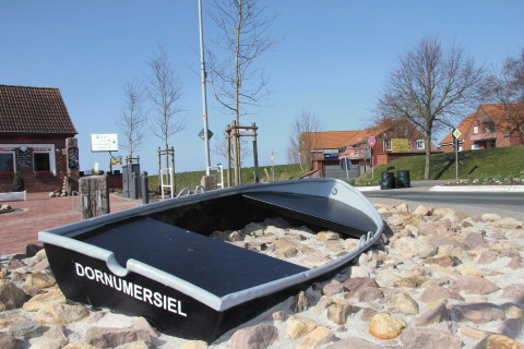 A small boat labeled 'Dornumersiel' rests on rocks near a road by Campingplatz am Nordseestrand glamping site.