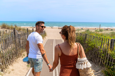 Pareja caminando de la mano hacia la playa en Camping Beauregard Plage - Glamping Languedoc-Roussillon.