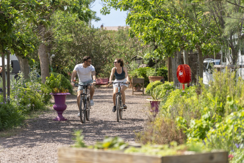 To personer cykler gennem grønne omgivelser på Camping Beauregard Plage - Glamping Languedoc-Roussillon.