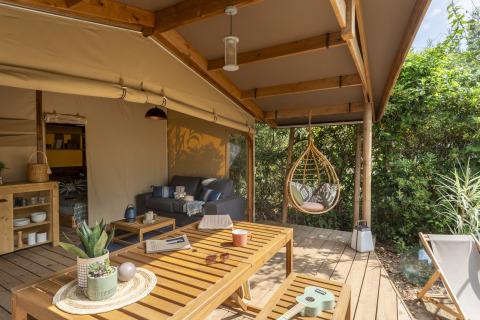 Terrazza esterna con sedia sospesa e arredi in legno al Camping Beauregard Plage Glamping in Linguadoca-Rossiglione.