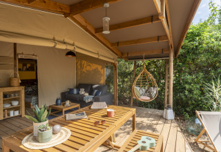 Buitenveranda met houten meubilair en hangstoel bij Camping Beauregard Plage Glamping in Languedoc-Roussillon.