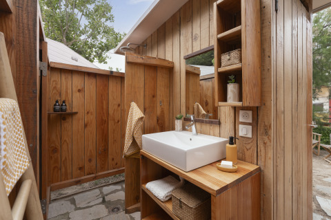 Outdoor wooden bathroom with sink, mirror and shelves at Camping Beauregard Plage, Glamping Languedoc-Roussillon.