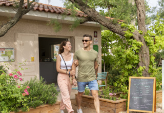 Happy couple walking outside their cabin at Camping Beauregard Plage - Glamping Languedoc-Roussillon, surrounded by greenery.