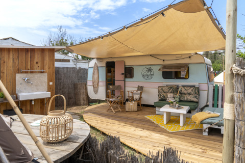Zona de glamping al aire libre con caravana retro, terraza de madera y área de descanso en Beauregard Plage.