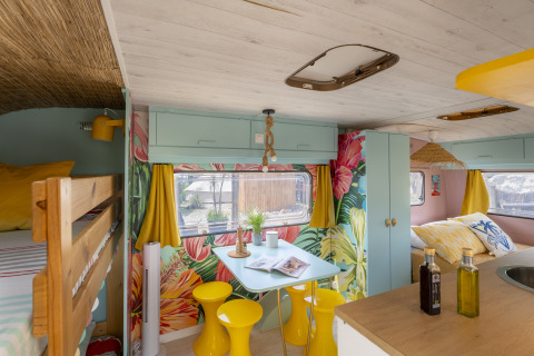 Farbenfrohes Glamping-Mobilheim mit Blumendekor, gelben Vorhängen und Essbereich im Languedoc-Roussillon.