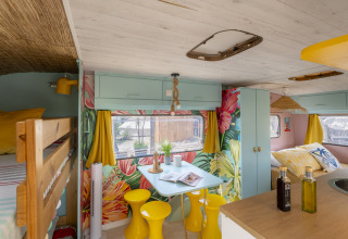 Indretning af en farverig glamping-vogn med blomstrede vægge, gule gardiner og spiseplads i Languedoc-Roussillon.