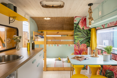 Kleurrijk glamping interieur met stapelbedden, eethoek en tropisch behang op Camping Beauregard Plage.