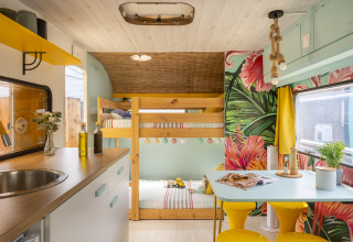 Intérieur de glamping coloré avec lits superposés, coin repas et papier peint tropical à Beauregard Plage.