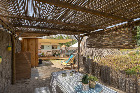 Udendørs glampingområde med overdækket terrasse, bord og stole nær campingvogn på Camping Beauregard Plage.