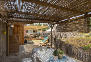 Zona de glamping al aire libre con techo de caña, mesa, sillas y caravana en Camping Beauregard Plage.