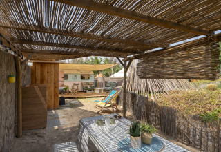 Overdekte glampingruimte met tafel, stoelen en ligstoelen bij een caravan op Camping Beauregard Plage.