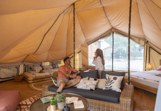 Vista interior de una lujosa tienda glamping en Camping Beauregard Plage, Languedoc-Roussillon, con huéspedes relajados.