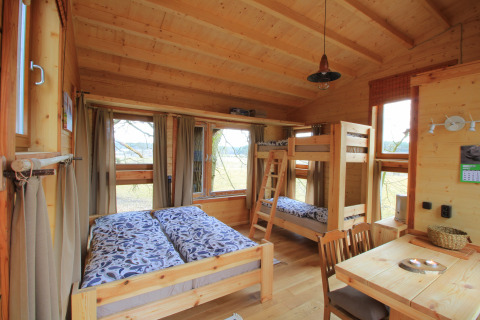 Agradable cabaña de madera con cama doble, literas y mesa de comedor en Boomhuthotel Uckermark.
