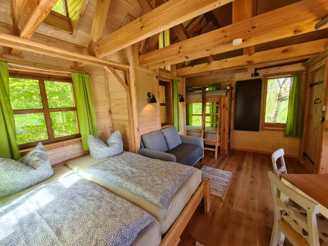 Intérieur chaleureux de cabane en bois pour glamping avec lits jumeaux et rideaux verts au Boomhuthotel Uckermark.