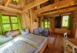 Gemütliches Baumhaus mit Holzbalken, Einzelbetten, Etagenbett und Sofa im Boomhuthotel Uckermark, Brandenburg.