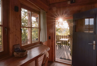 Zicht vanuit een gezellige houten boomhut op het zonovergoten terras bij Boomhuthotel Uckermark, Brandenburg.