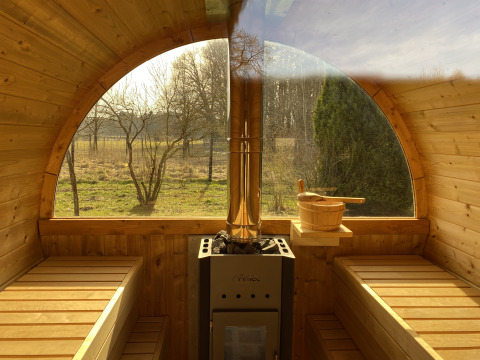 Interior view of a wooden barrel sauna with large windows, wooden benches and stove at Boomhuthotel Uckermark.