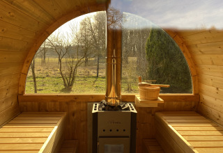 Indvendig udsigt af en trætønde-sauna med store vinduer, træbænke og brændeovn i Boomhuthotel Uckermark.