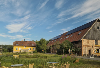 Glamping accommodation at Boomhuthotel Uckermark in Brandenburg with farm buildings by a pond and garden.