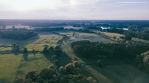 Luftaufnahme vom Boomhuthotel Uckermark Glamping in Brandenburg mit weiten Feldern und Wäldern im Sonnenlicht.