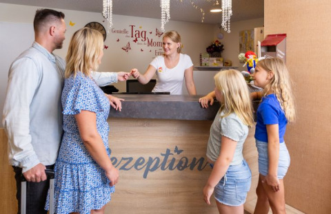 Een gezin checkt in bij de receptie van Camping Rhön Feeling - Tiny Houses Thüringen, glampingverblijf.