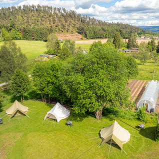 Aerial view of glamping tents at Les Jardins de Biffontaine surrounded by lush fields, trees and a greenhouse.