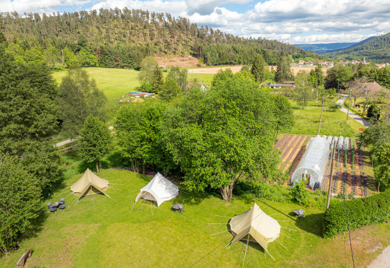 Vue aérienne des tentes glamping aux Jardins de Biffontaine, entourées de verdure et d’une serre maraîchère.