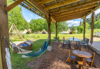 Zona de glamping en Les Jardins de Biffontaine con tiendas, hamaca y área de juegos bajo pérgola de madera.