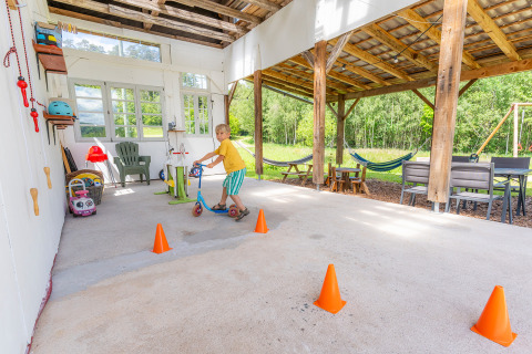 Bambino su monopattino tra coni arancioni sotto il portico di Les Jardins de Biffontaine glamping nei Vosgi.