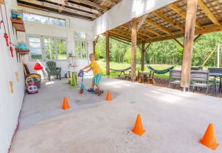 Bambino su monopattino tra coni arancioni sotto il portico di Les Jardins de Biffontaine glamping nei Vosgi.