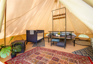 Interior de tienda glamping con alfombras, cama y plantas en Les Jardins de Biffontaine, Glampingtenten Vogezen.
