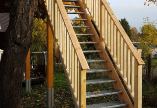 Trap naar een boomhut bij Boomhut Wesertal - Boomhutten Hessen glamping, tussen afgevallen herfstbladeren.