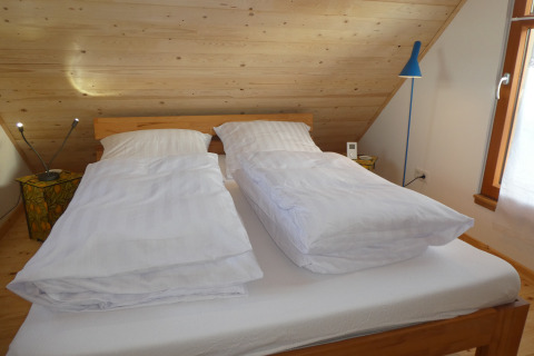 Slaapruimte in Boomhut Wesertal - Boomhutten Hessen met twee enkele donsdekens op een dubbel bed onder het dak.