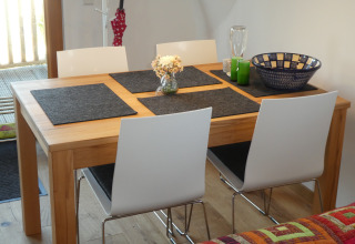 Essbereich mit Holztisch, weißen Stühlen und Dekoration in der Glamping-Unterkunft Boomhut Wesertal - Boomhutten Hessen.