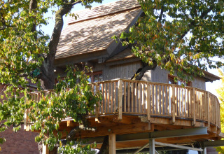 Alloggio glamping in casa sull’albero a Hessen con terrazza in legno e circondato da alberi verdi.