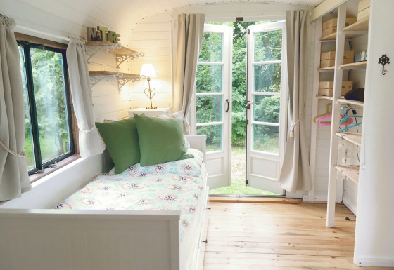 Lyst og hyggeligt interiør i en glampingvogn med åbne dobbeltdøre mod en grøn have i Gesundheidshof Denker.