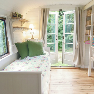 Intérieur clair et cosy d'une roulotte de glamping avec portes-fenêtres ouvertes sur un jardin chez Gesundheidshof Denker.