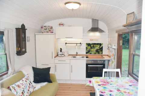 Acogedor interior del Zigeunerwagen Jutland glamping con cocina, sofá y comedor en Gesundheitshof Denker.
