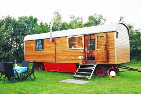 Charming glamping accommodation in a wooden wagon with outdoor seating, set on a lush green lawn.