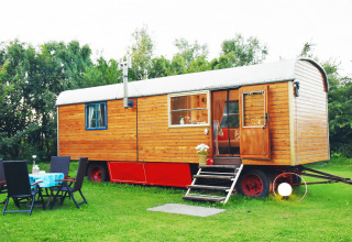 Gezellige glamping-wagen van hout met zithoek in de tuin, geplaatst op een frisgroen grasveld.
