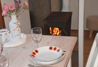 Tavola accogliente con fiori, piatti e camino sullo sfondo nel carro da glamping Jutland.